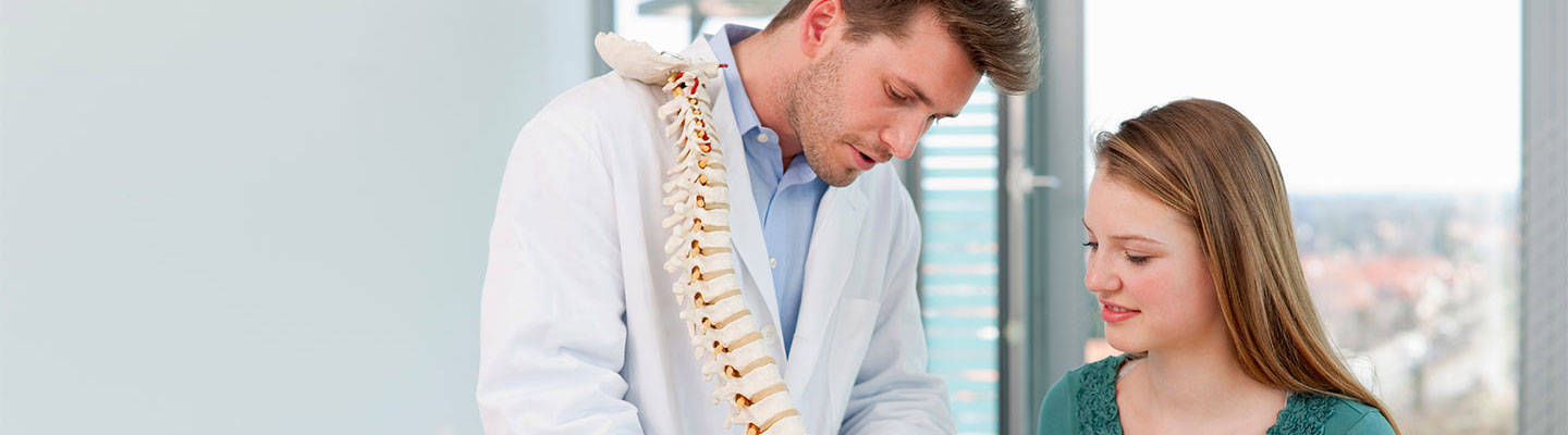 Un proveedor de salud demuestra lesiones en la columna vertebral a un paciente utilizando un modelo.