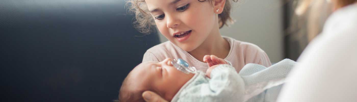 Hermana mayor conociendo a un nuevo bebé en el hospital por primera vez.