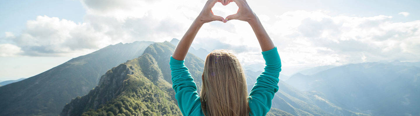 Mujer formando corazón con las manos y mirando la montaña