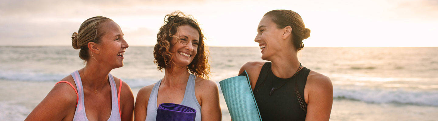 3 mujeres que llevan colchoneta de yoga en la playa