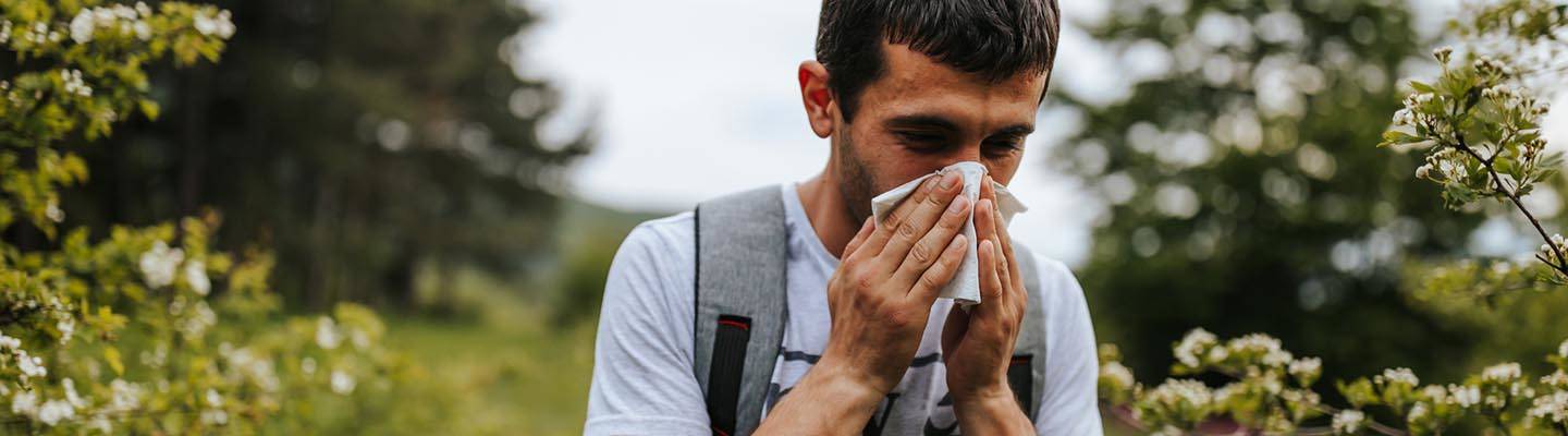 Hombre con alergia al polen estornudando en el campo