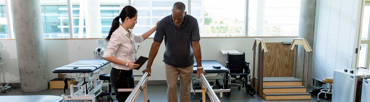 Terapeuta ayuda a un hombre a caminar sobre barras paralelas